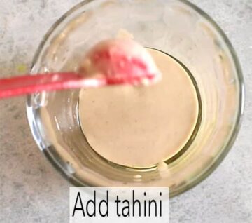 A red measuring spoon adding tahini to mixing bowl
