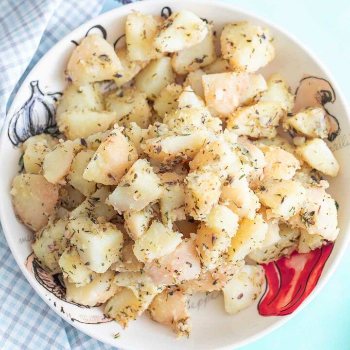 Top view of a white bowl on a blue background. Bowl filled with potato salad.