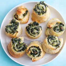 Top view of 8 puff pastry pinwheels on a white plate and a blue background.