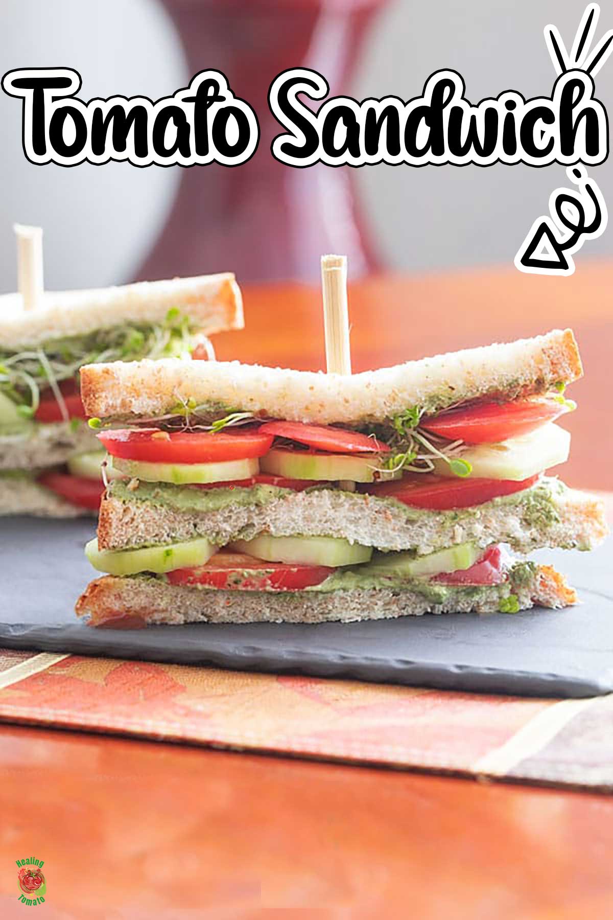 Front view of a double decker tomato sandwich with layers of tomato, cucumber, pesto spread and broccoli sprouts
