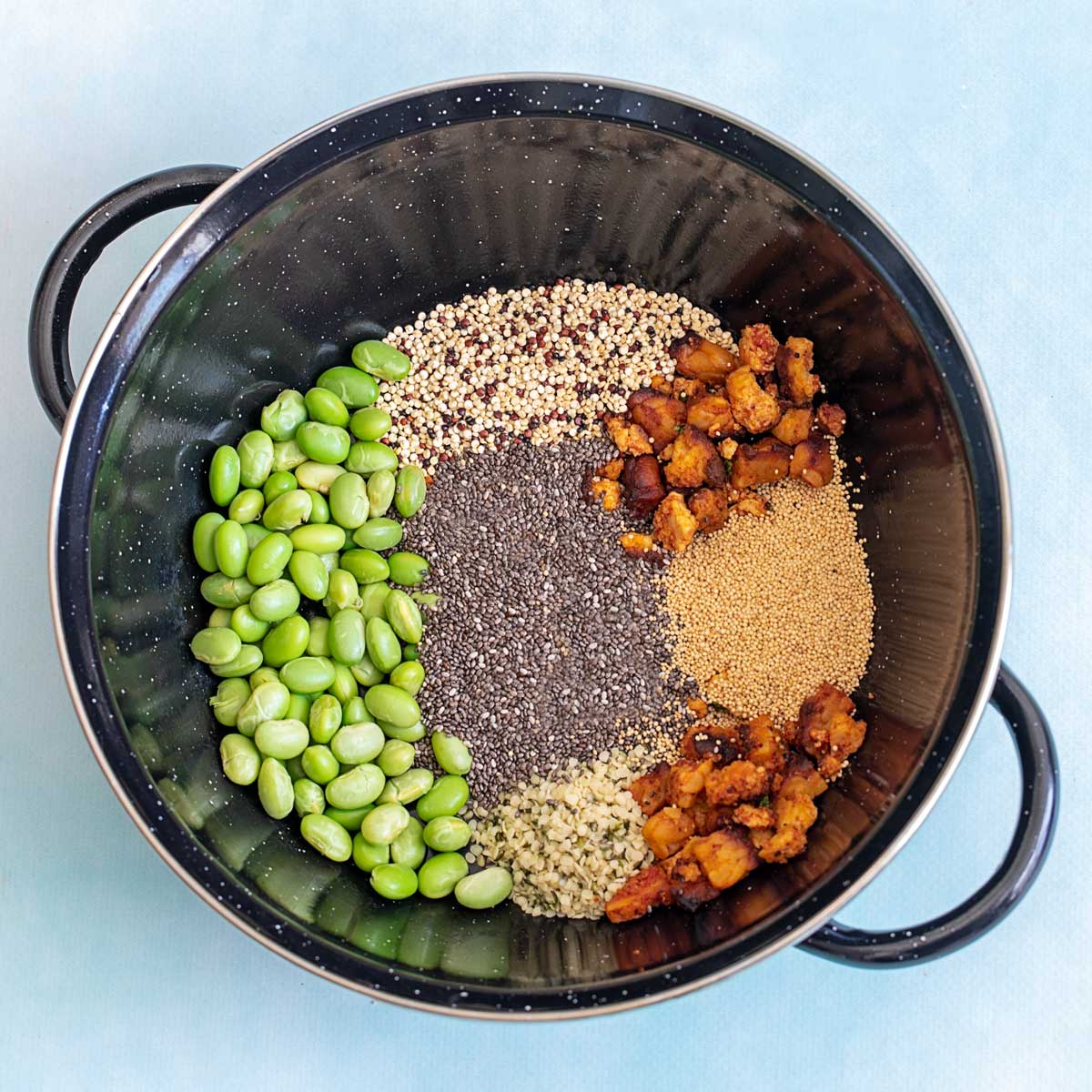 Top view of a black wok filled with edamame, chia seeds, hemp seeds, quinoa, amaranth and tofu crumbles.