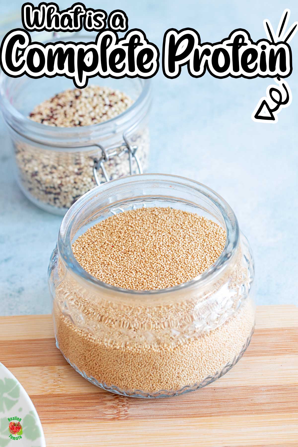 front view of a glass jar filled with amarnth grain. Quinoa can be seen in the background