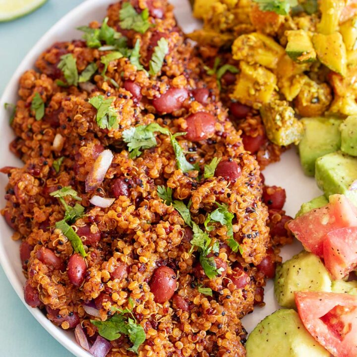 Top view of a white plate with quinoa and red beans on one side. An avocado and tomato salad on the other side