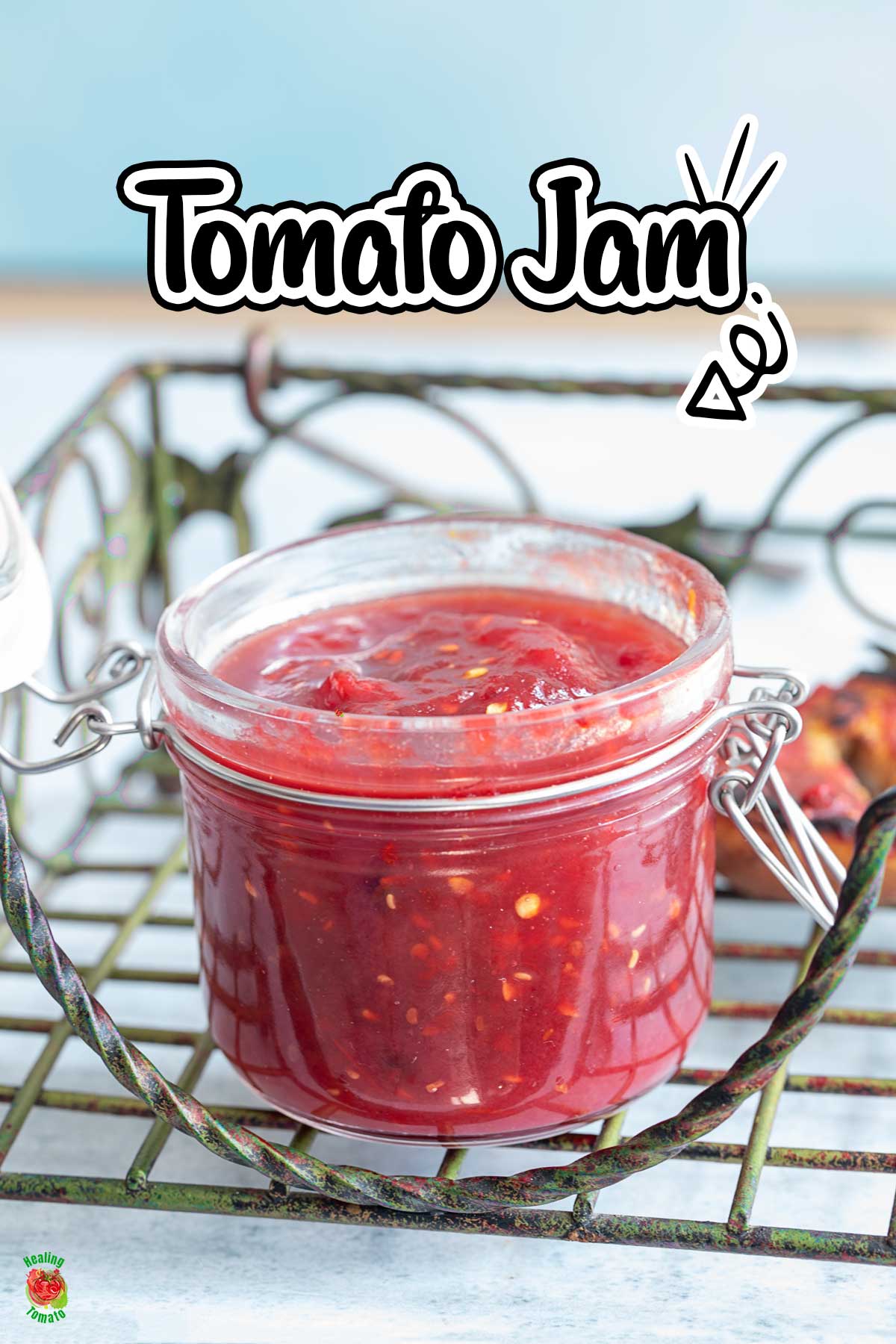 Front view of a glass jar filled with tomato jam on a green iron tray