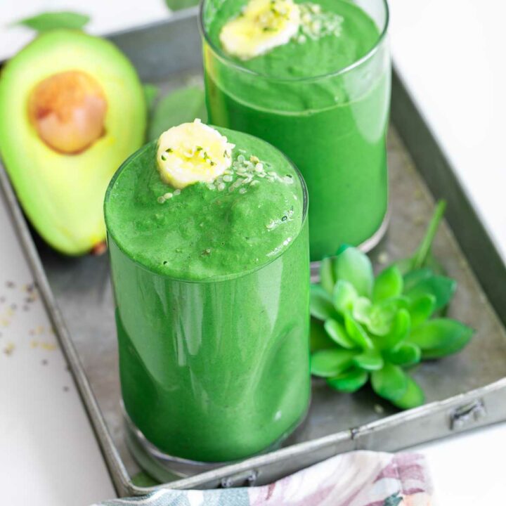 Top and angle view of a glass filled with green smoothie. A second glass is in the background too.