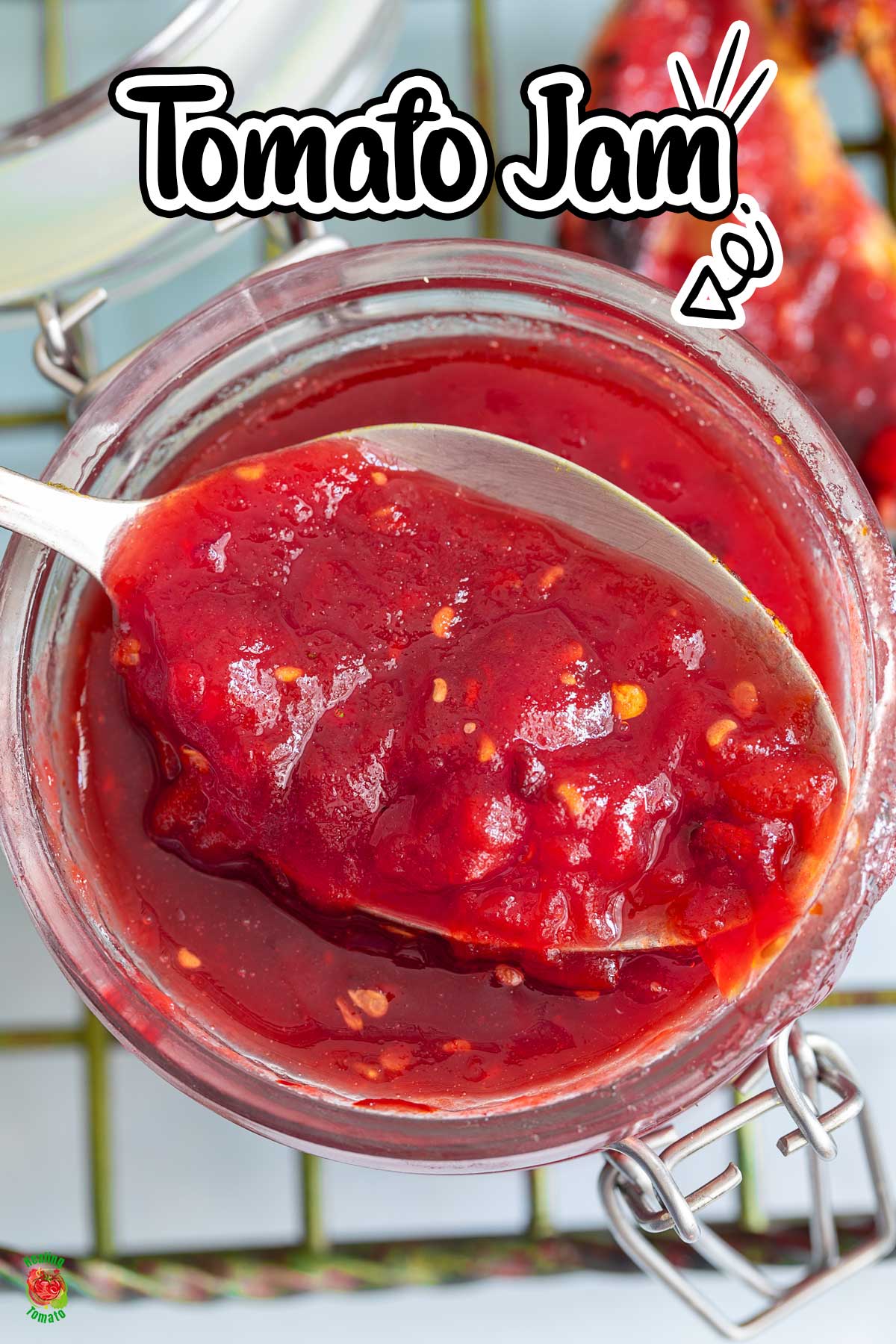 Top view of a spoon with tomato jam resting on the top of a glass jar.