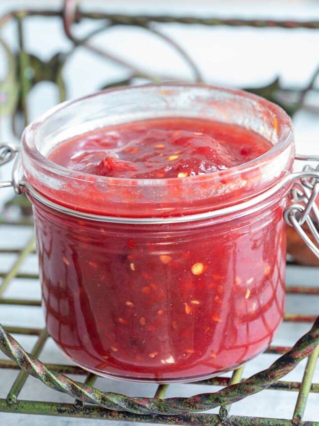 Front view of a glass jar filled with tomato jam on a green iron tray