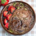 Top and closeup view of a brown wooden bowl filled with vegan chocolate smoothie. Garnish of strawberries, seeds and matcha powder.