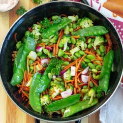 Top and closeup view of a small black wok filled with stir fry vegetables.