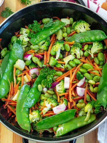 Top and closeup view of a small black wok filled with stir fry vegetables.