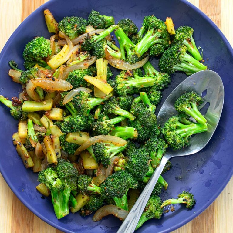 Top and closeup view of cooked broccoli and onions on a blue plate with a steel serving spoon
