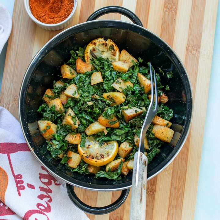 Top view of a black wok filled with sauteed kale and potatoes. Wok is on a brown chopping board