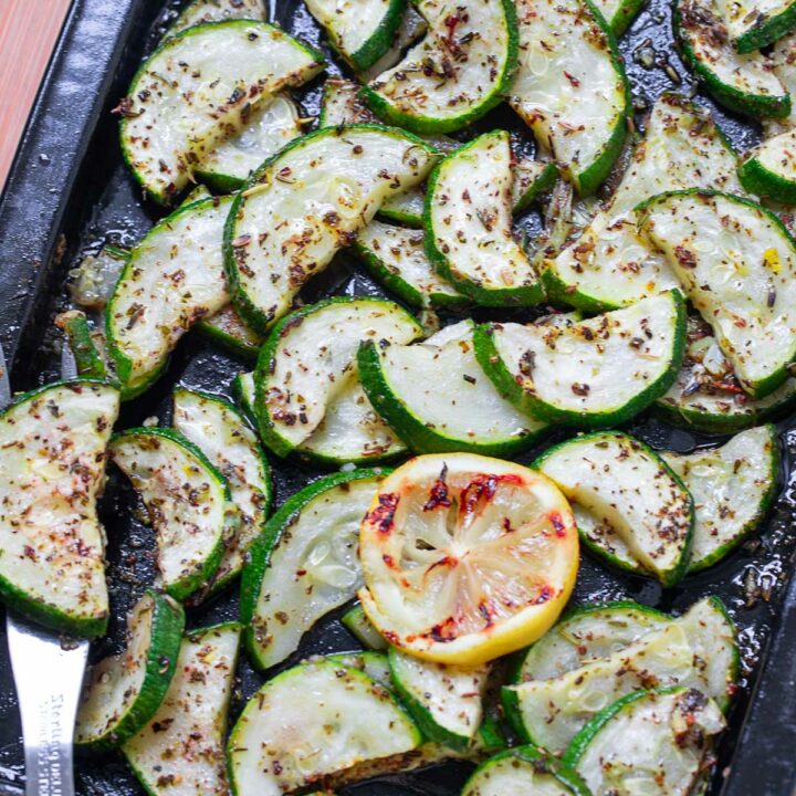 Top view of roasted zucchini in a sheet pan with grilled lemon slices for garnish