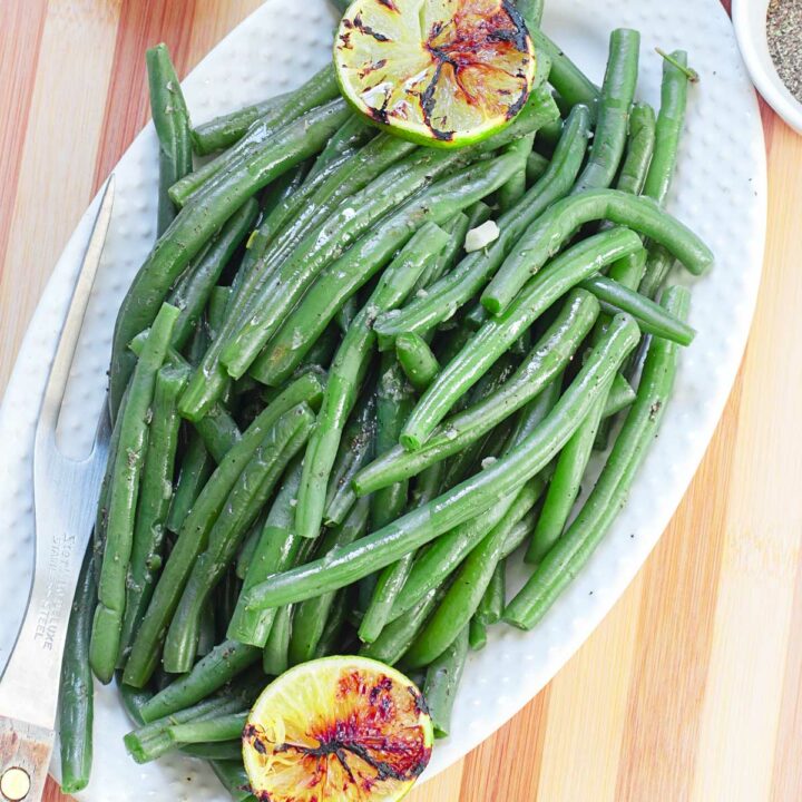 Top and closeup view of green beans in a white serving dish placed on a brown cutting board