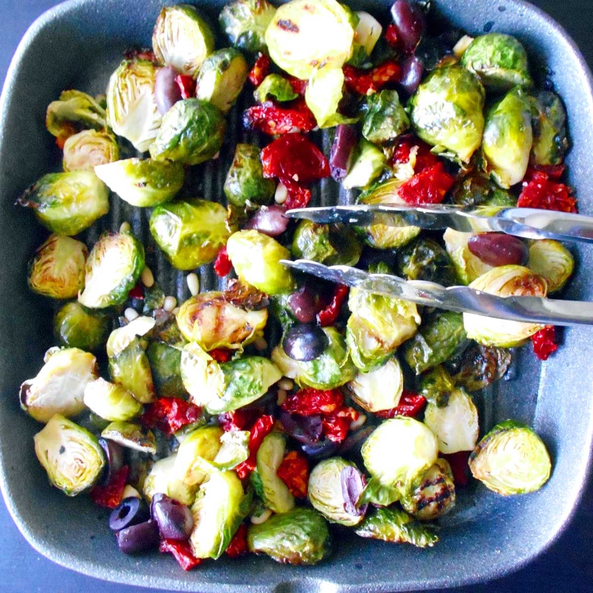 Top view of cooked Mediterranean Brussels sprouts in a grey square skillet.