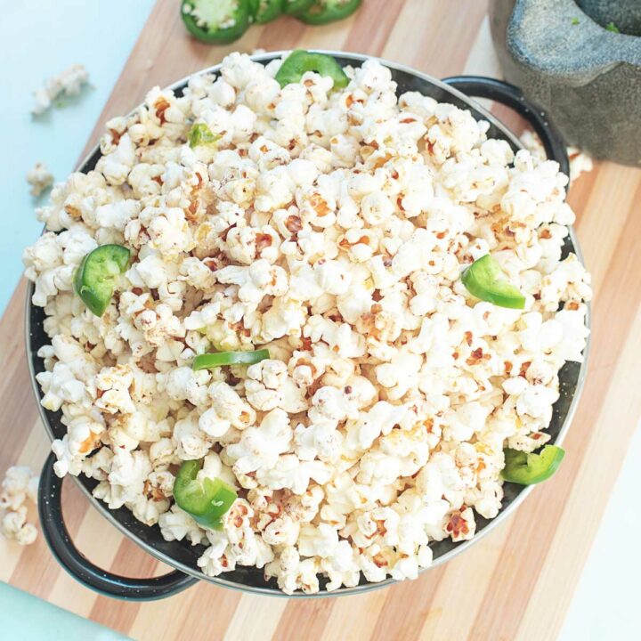 Top view of popcorn in a black pan. Pieces of jalapeño slices as garnish.