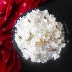 top view of a dark bowl filled with white rice. An Indian scarf is on the side