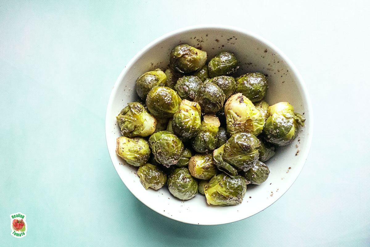 Top view of a white bowl filled with cooked Brussels Sprouts.